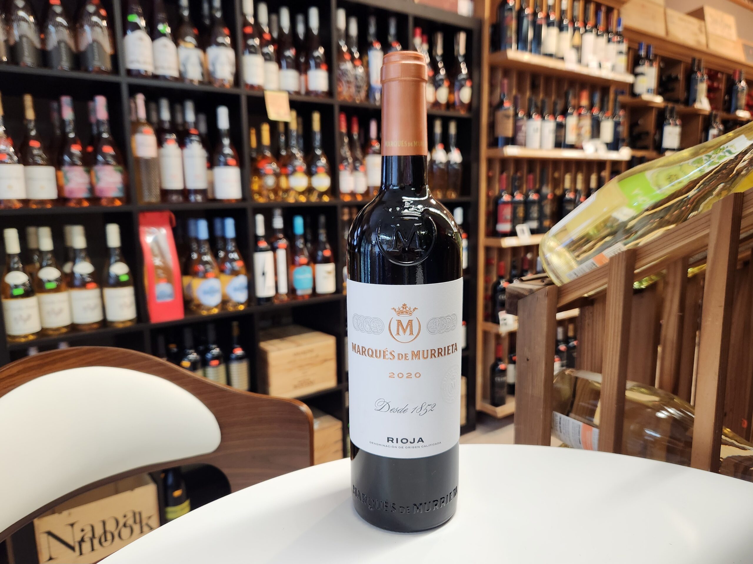 ChatGPT said: Absolutely! Here’s clean, descriptive alt text for the image: A bottle of Marqués de Murrieta Rioja Reserva 2020 displayed on a white table inside a wine shop, with shelves of bottles in the background.